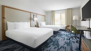 A hotel room with two beds, a desk, a chair, a TV, and a window with curtains.