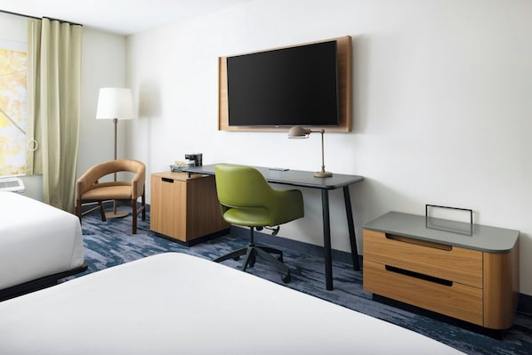 Une chambre d’hôtel avec un lit, un bureau, une chaise et un téléviseur fixé au mur.