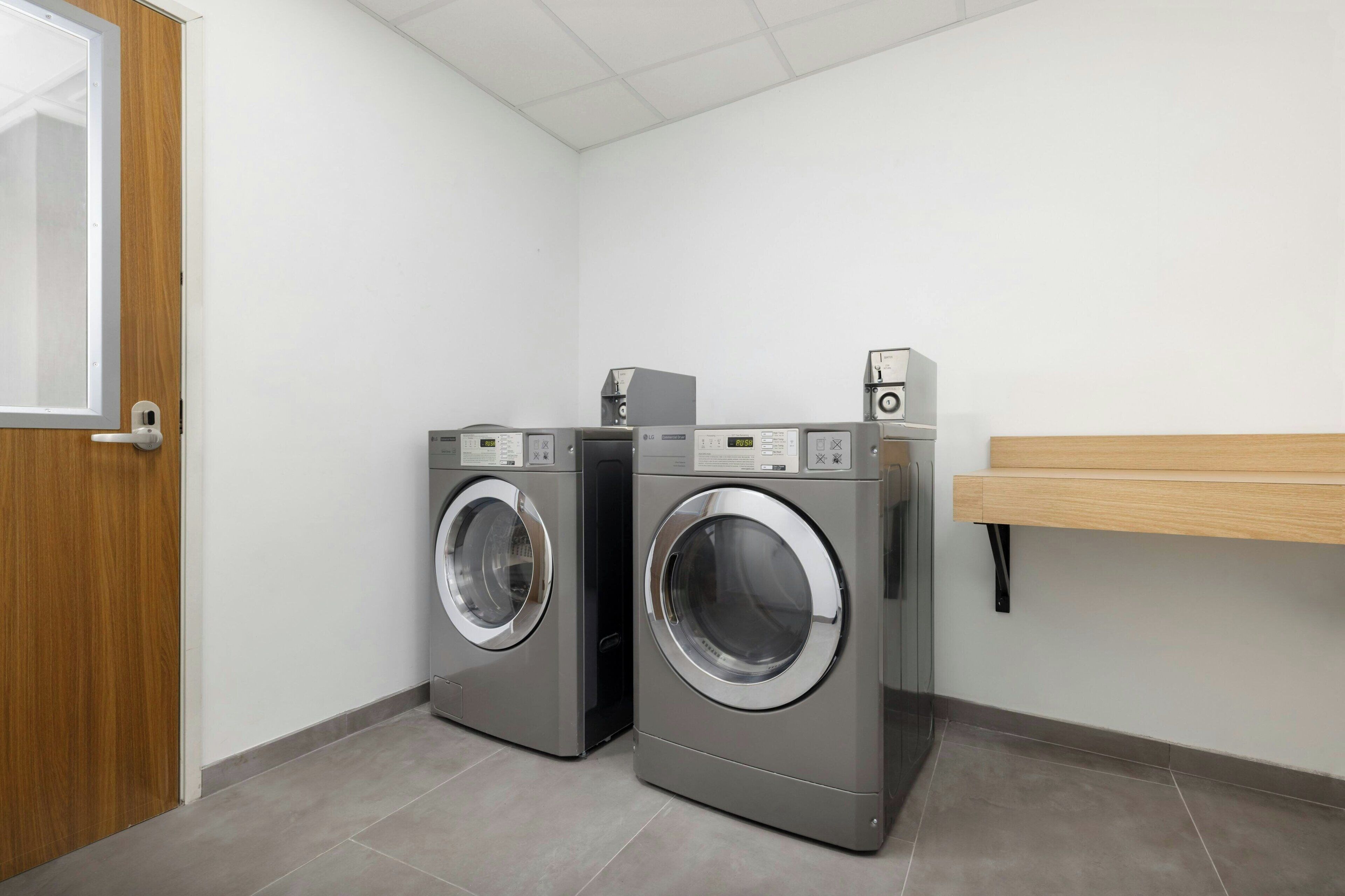 A laundry room with two front-loading washing machines and a dryer, a wooden door, and a white wall.
