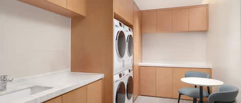 A compact kitchen with a built-in washer and dryer, a sink, and a small dining area with chairs.