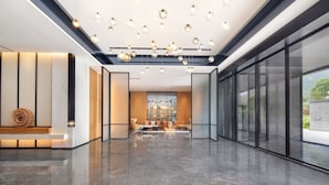A spacious lobby with a modern design, featuring a marble floor, contemporary furniture, and a ceiling with hanging spherical lights.