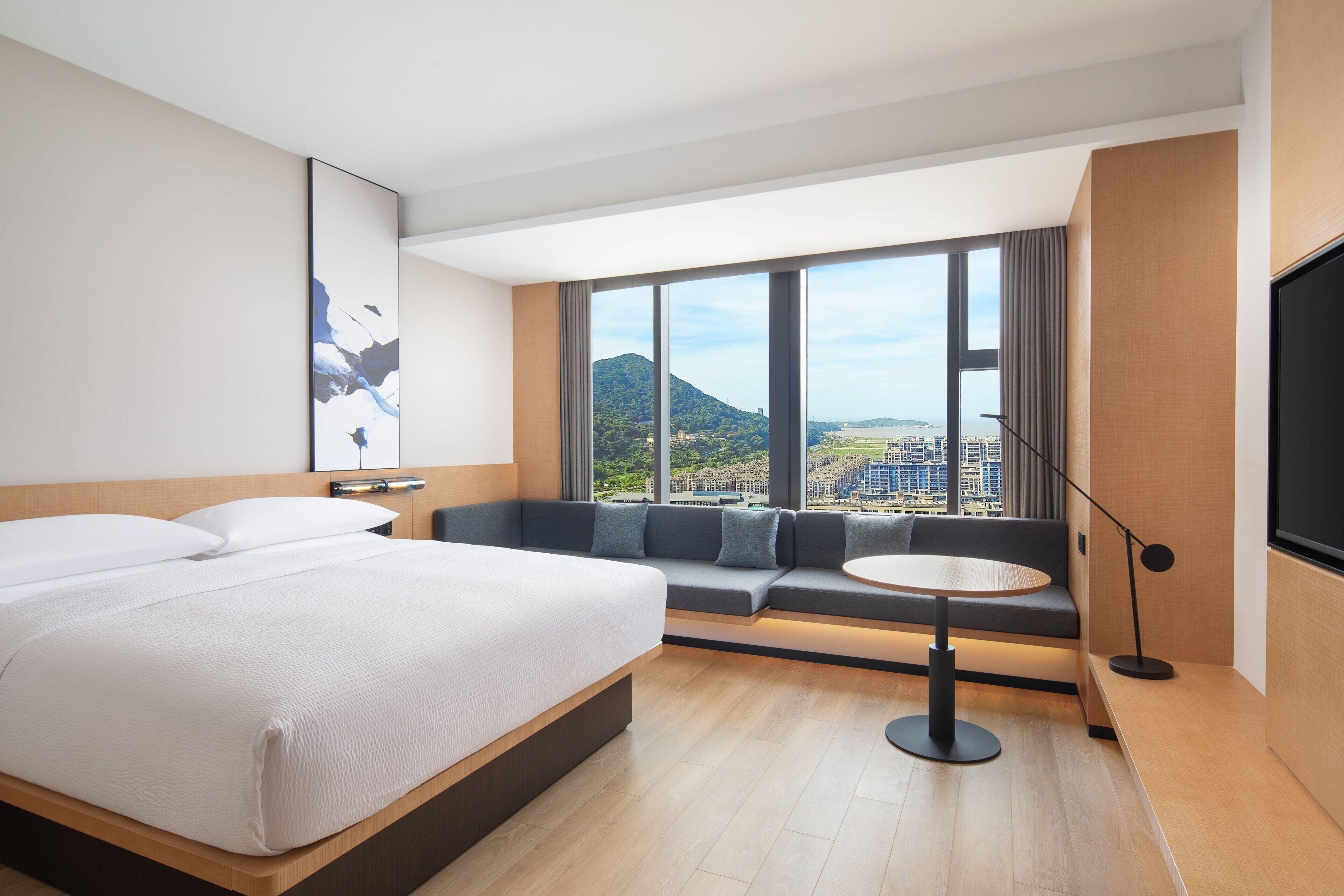 Una habitación de hotel moderna con una cama grande, un sofá, una mesita y un televisor.