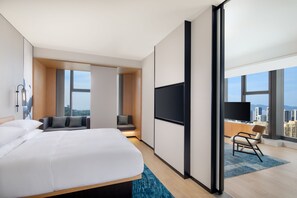 Et moderne hotelværelse med en stor seng, et opholdsområde med fjernsyn og udsigt over byen.