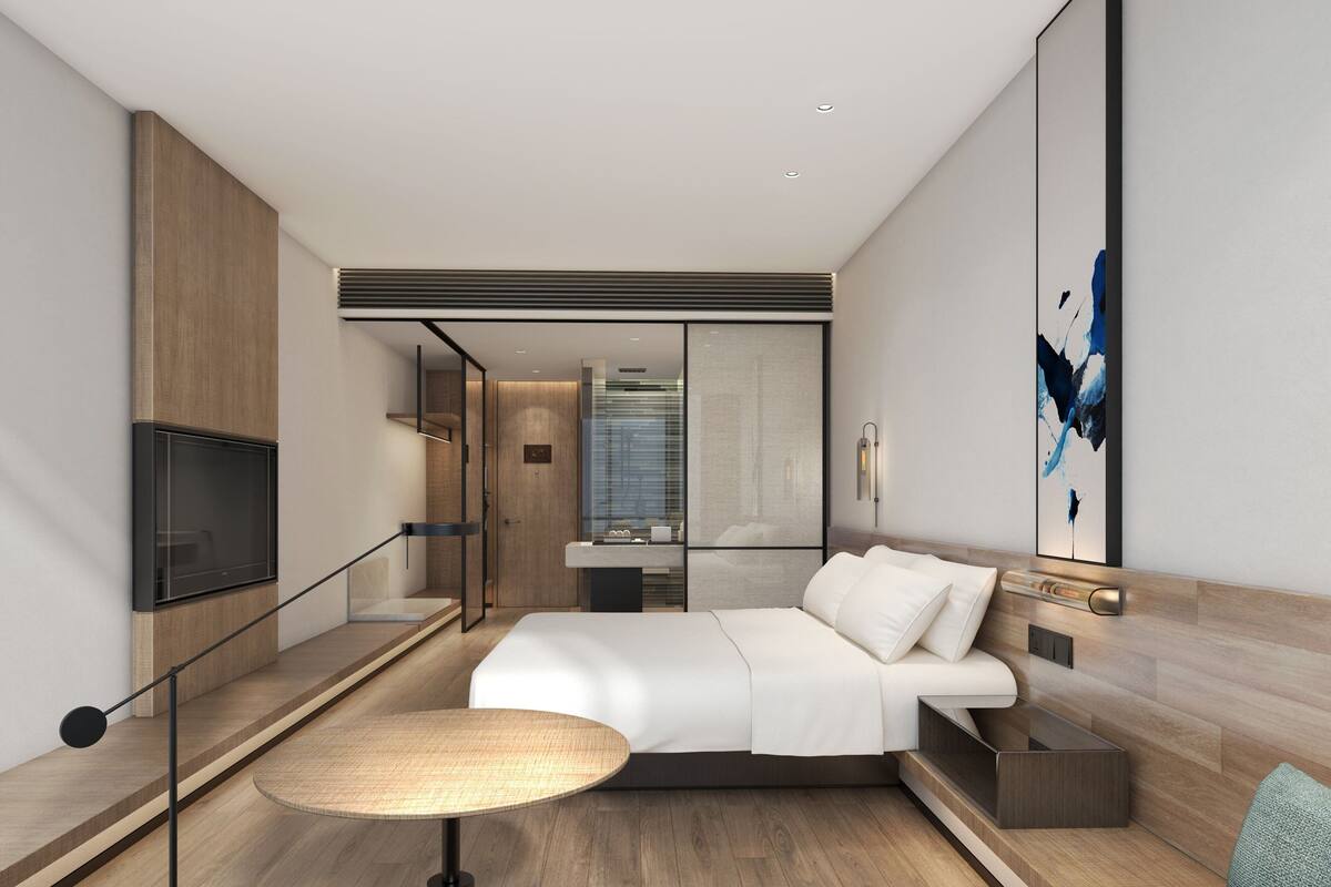 Ein modernes Hotelzimmer mit einem Bett, einem Nachttisch und einem großen Fenster.