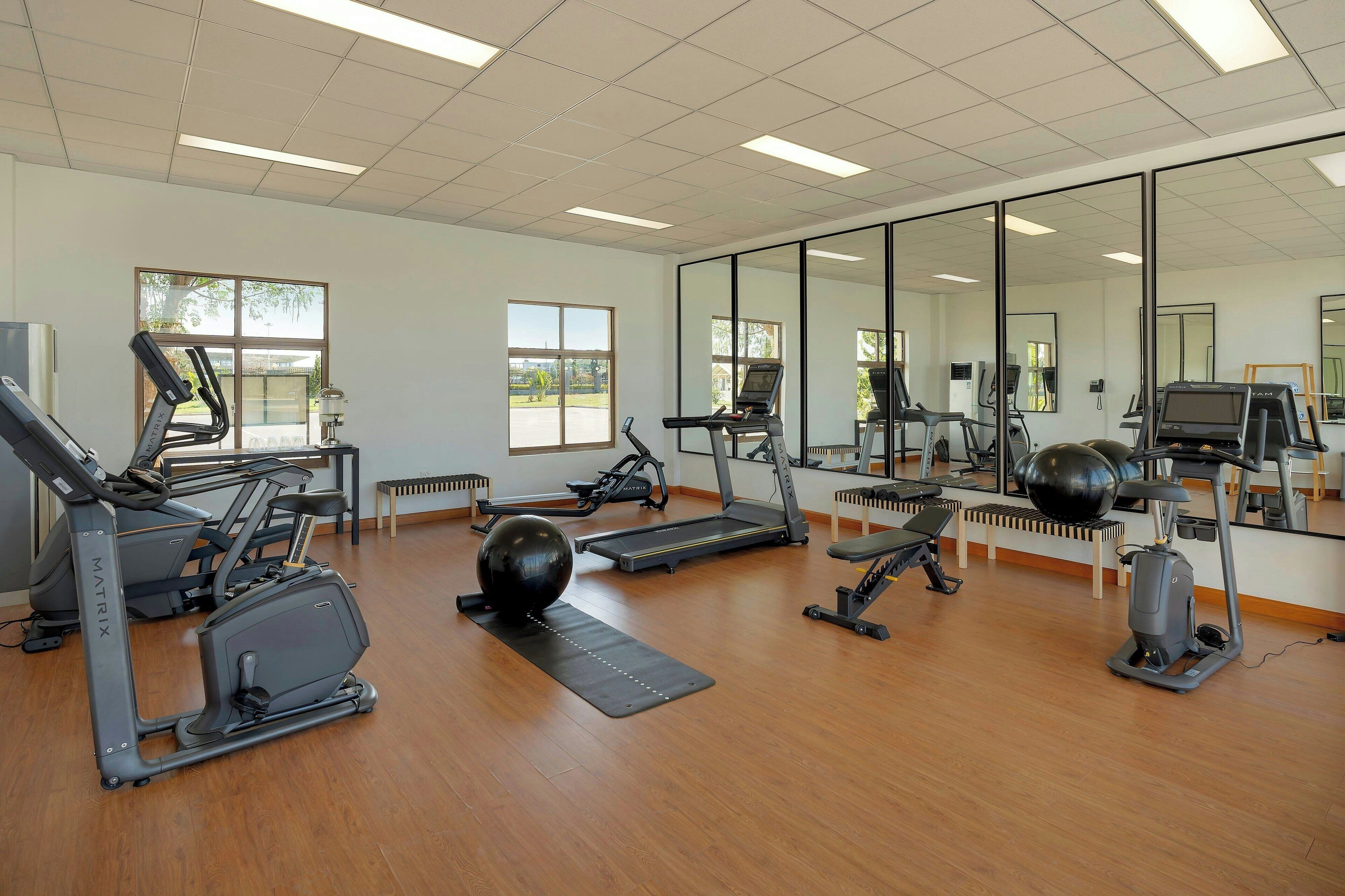 A gym with various exercise equipment, large windows, and a mirrored wall.