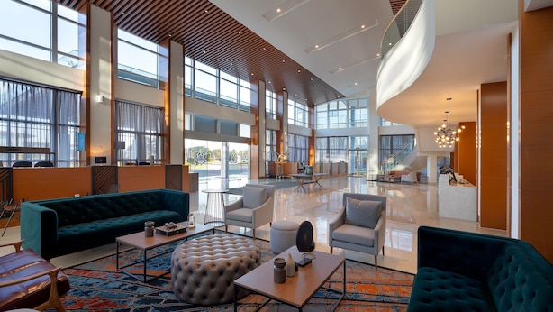 A spacious lobby with a high ceiling, large windows, and modern furniture including sofas and armchairs.