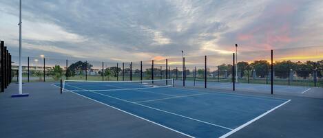 Ein Tennisplatz im Freien mit Netz, umgeben von einem Zaun, unter einem bewölkten Himmel.
