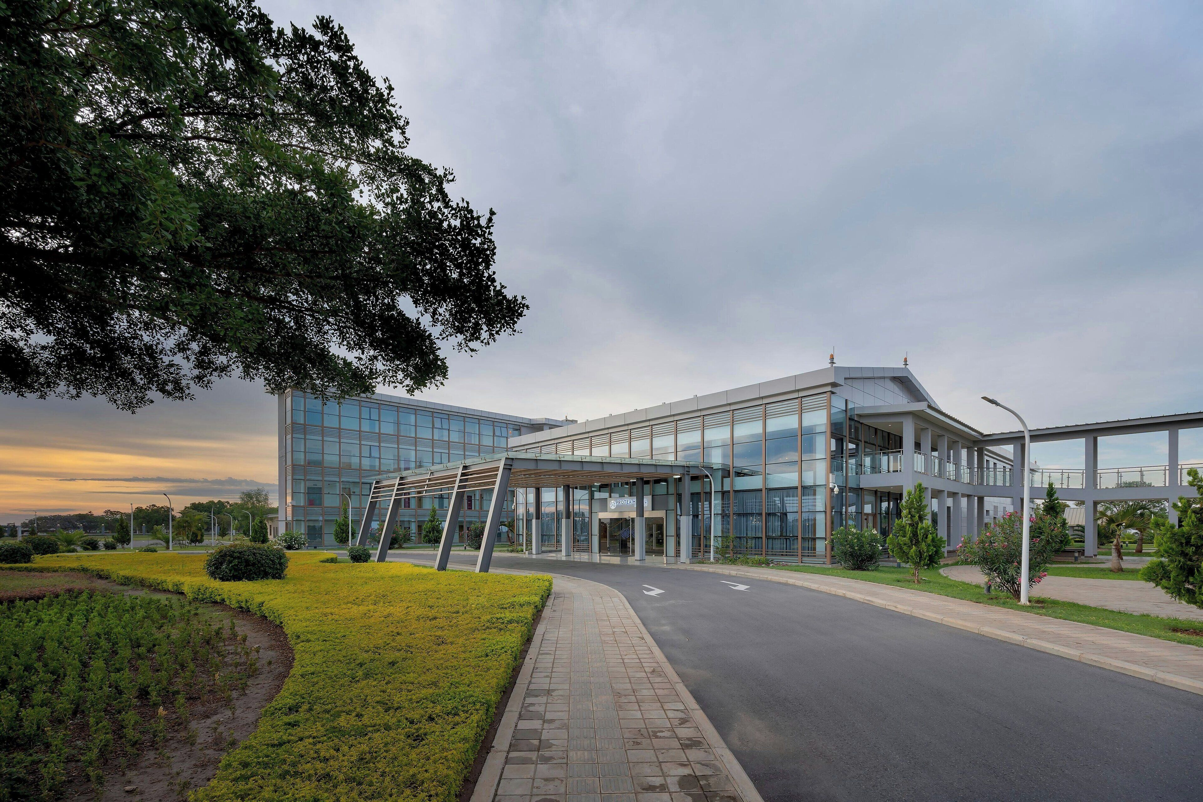 A modern building with a glass facade, a covered entrance, and a landscaped area with a pathway leading to the entrance.