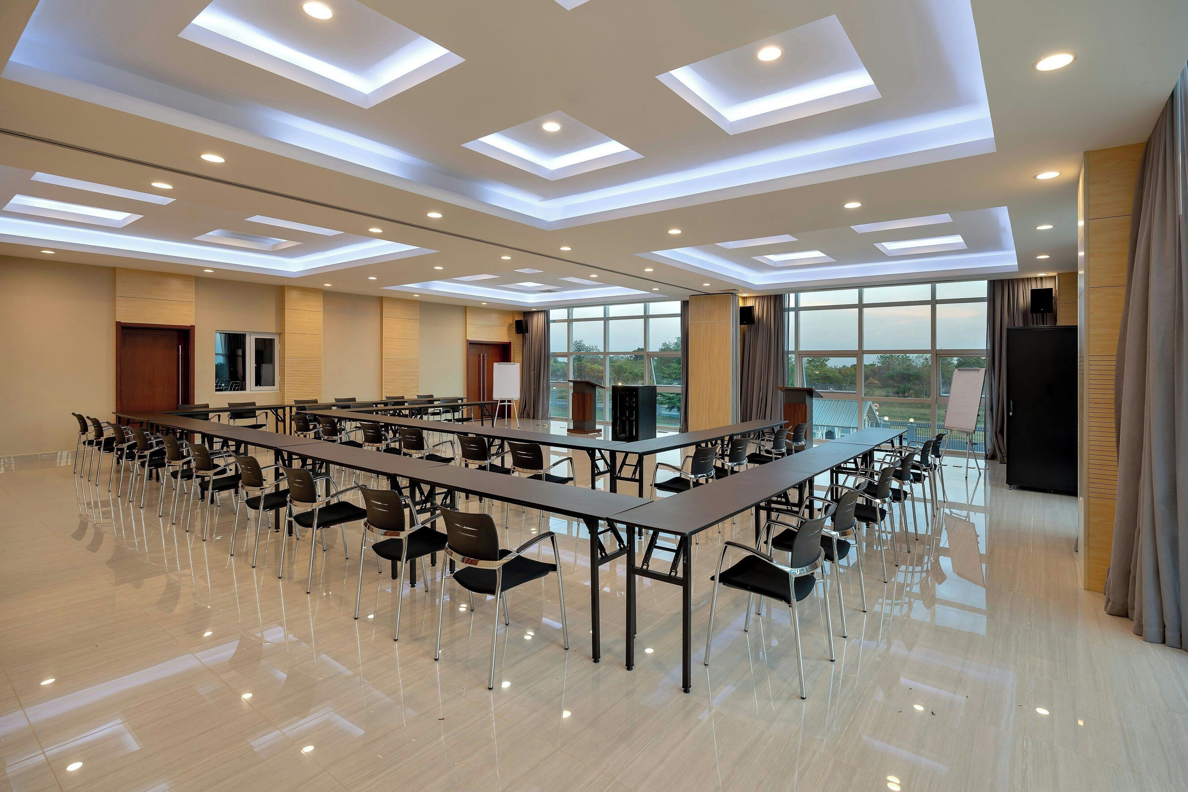 A spacious conference room with long tables, chairs, and a large window providing a view of the outdoors.