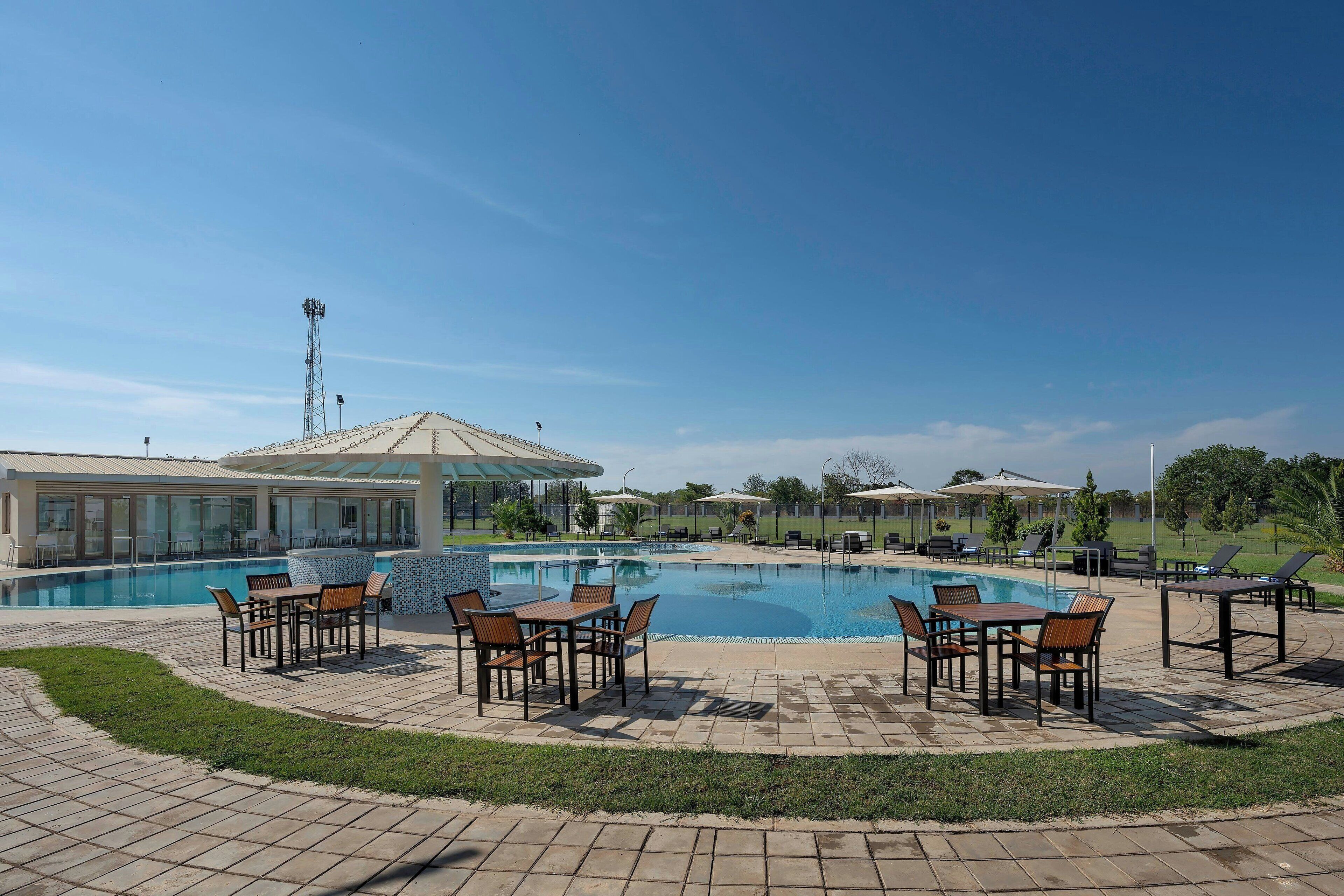 Una piscina con sillones de descanso y sombrillas, rodeada de jardines y un edificio al fondo.