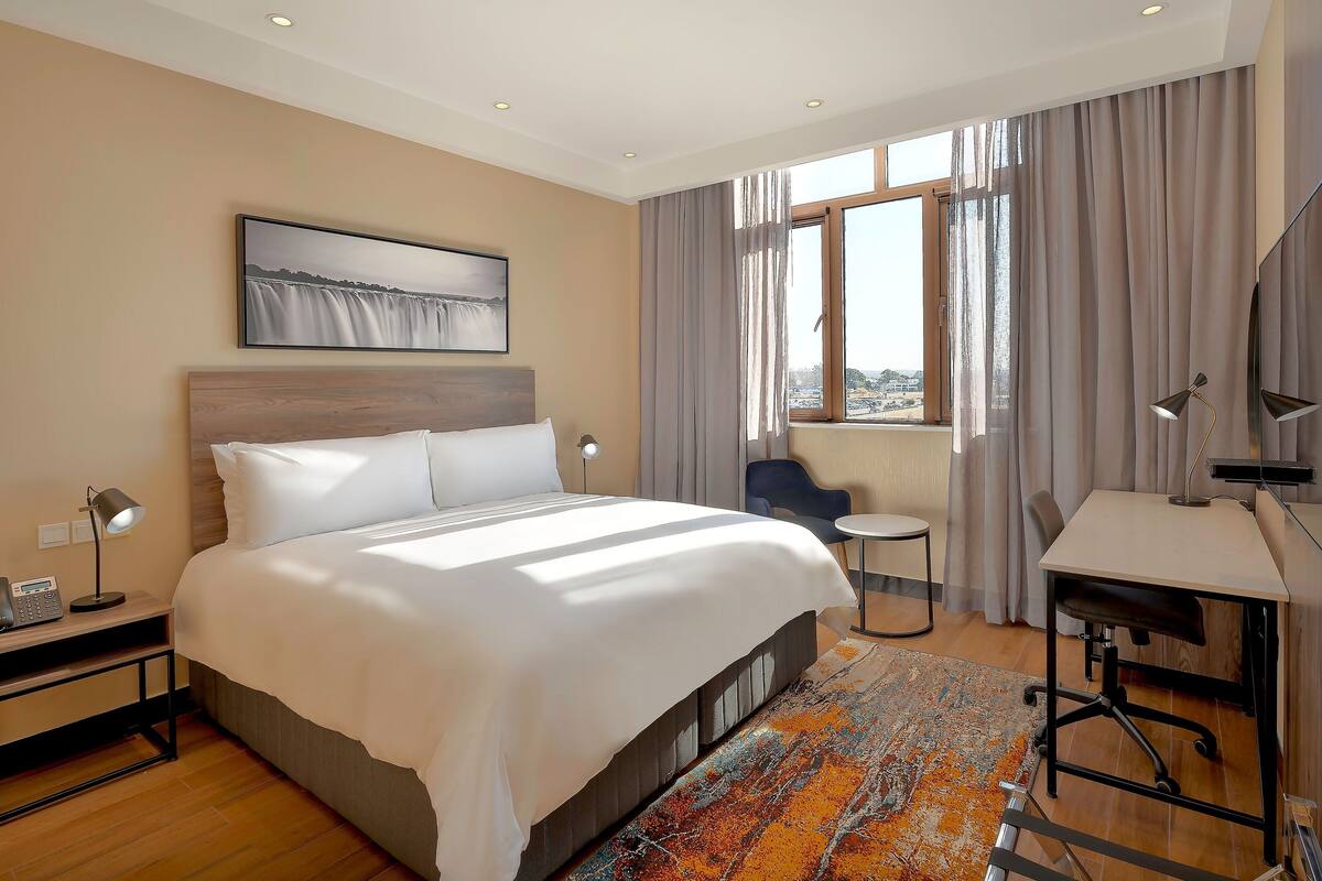 Habitación de hotel con una cama grande, un escritorio, una silla, una mesita y una ventana con cortinas.