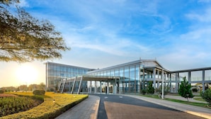 A modern building with a glass facade, a covered entrance, and a landscaped area with a pathway and greenery.