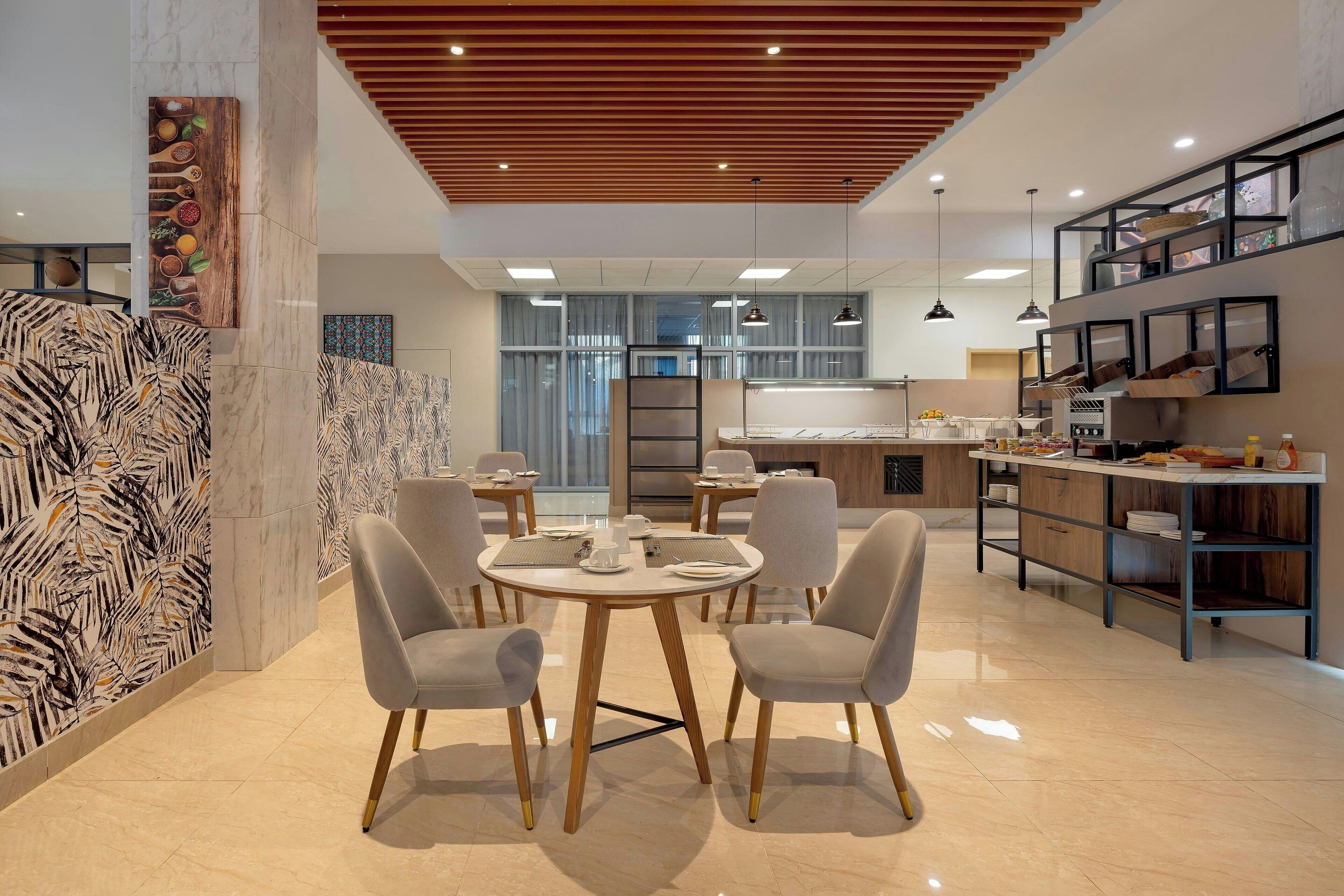 A modern dining area with round tables and chairs, a kitchen with a built-in island, and a view of the city through large windows.