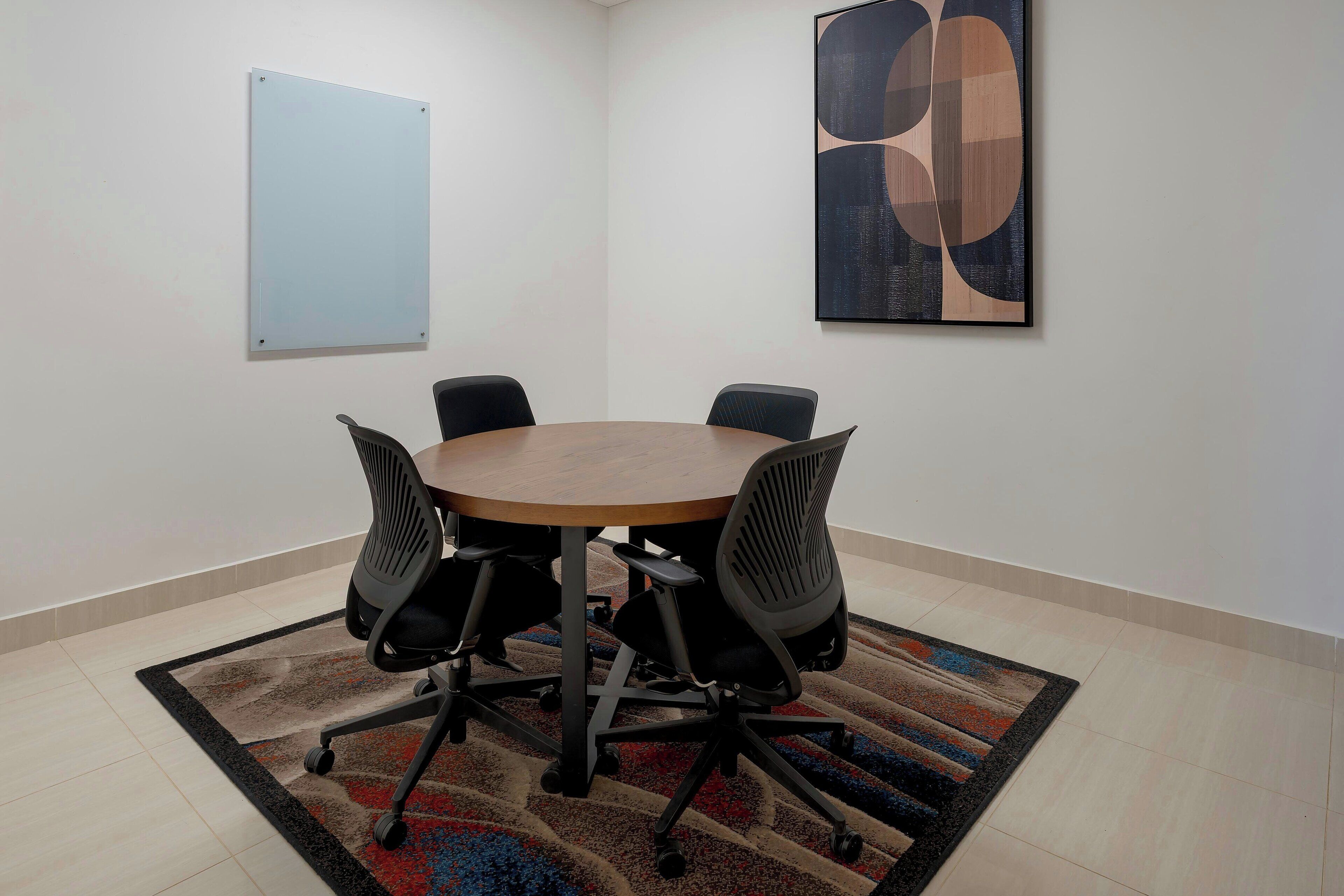 A conference room with a round table, four chairs, a whiteboard, and a large abstract painting on the wall.