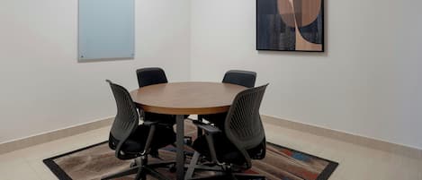 A conference room with a round table, four chairs, a whiteboard, and a large abstract painting on the wall.