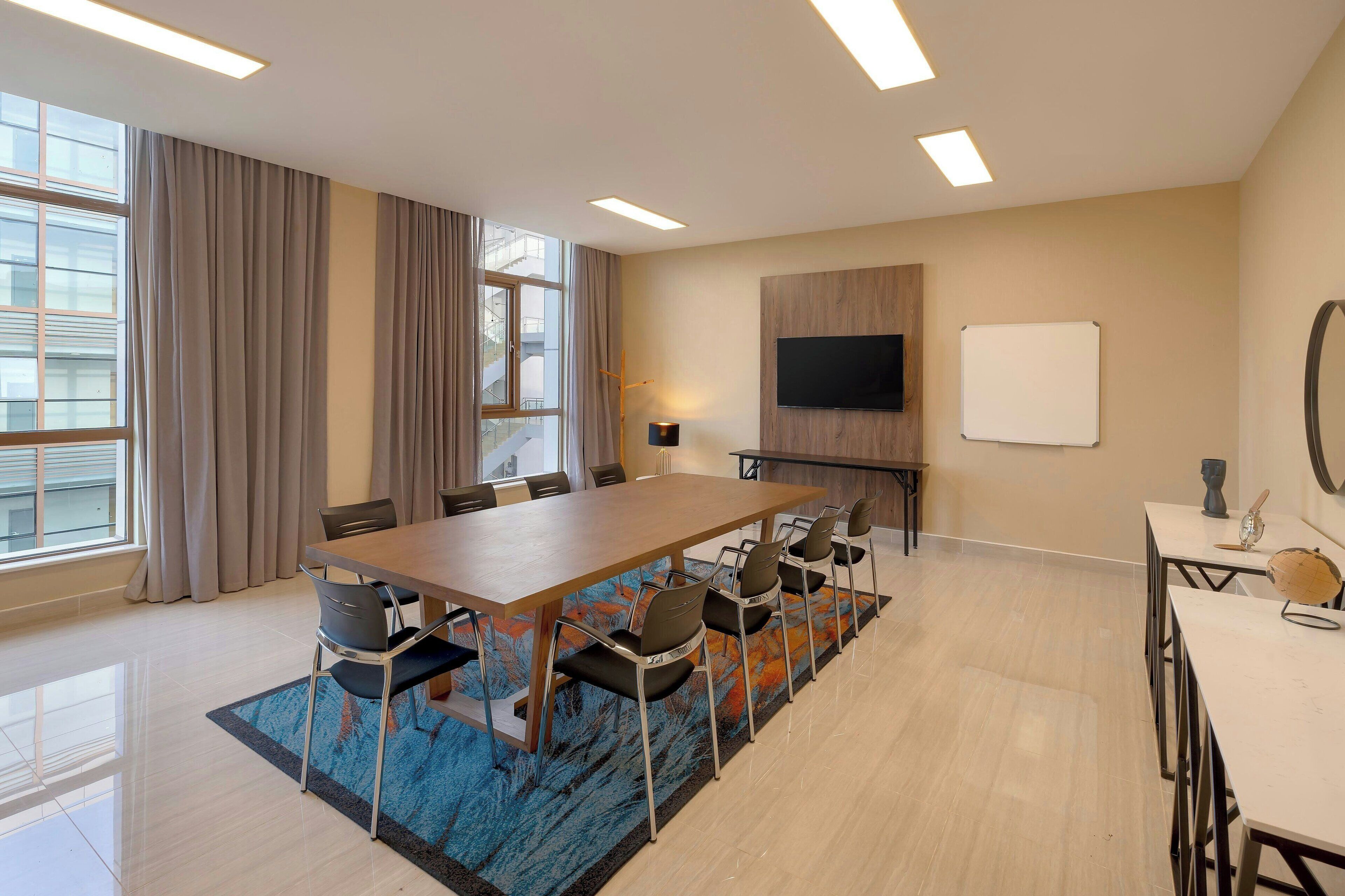 A conference room with a long table, chairs, a TV, and a whiteboard.