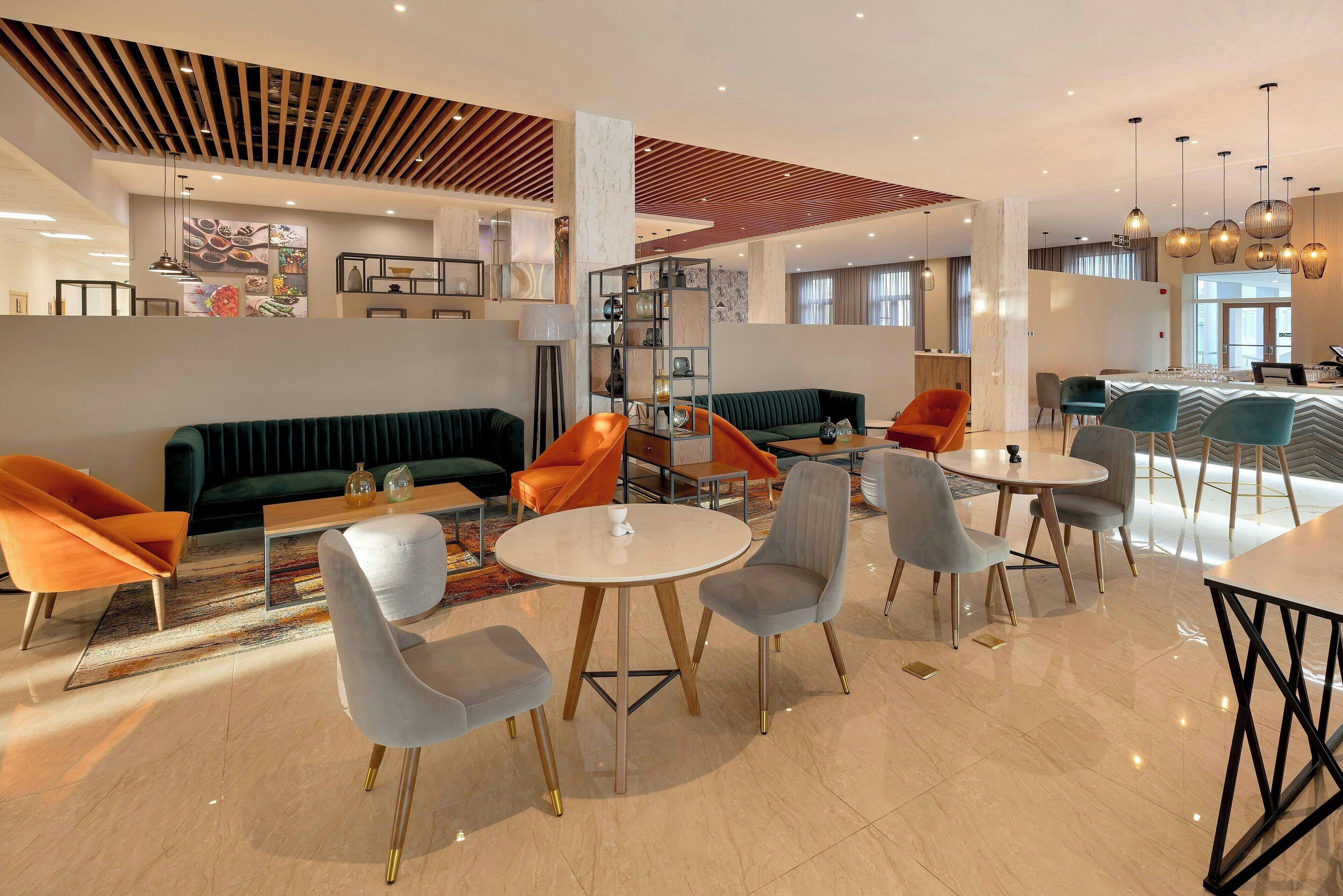 Un vestíbulo de hotel moderno con un sofá verde, sillas naranjas y una mesa redonda.