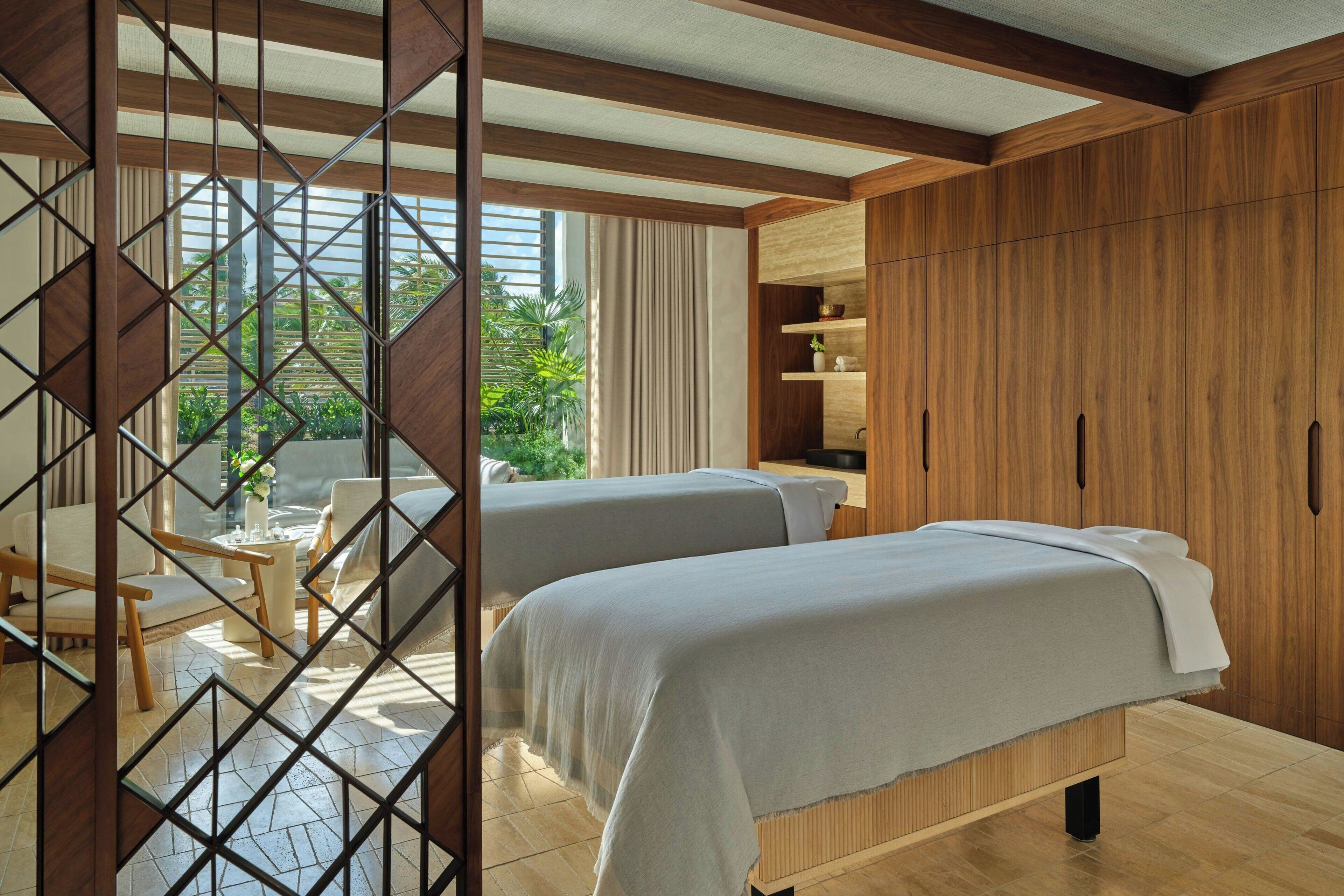 A hotel room with two beds, wooden furniture, a view of greenery, and a large wardrobe.