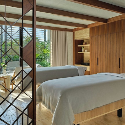 A hotel room with two beds, wooden furniture, a view of greenery, and a large wardrobe.