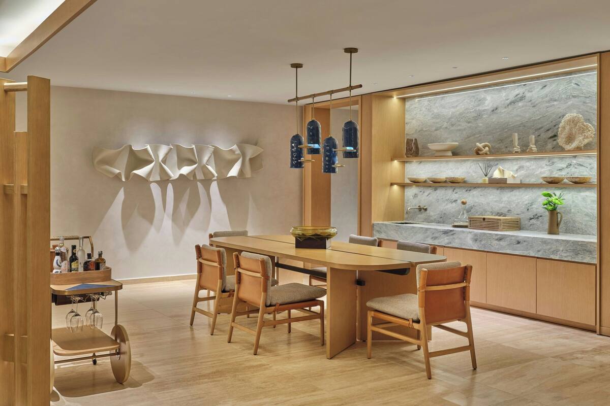 A modern kitchen with a wooden dining table, chairs, and a marble countertop.