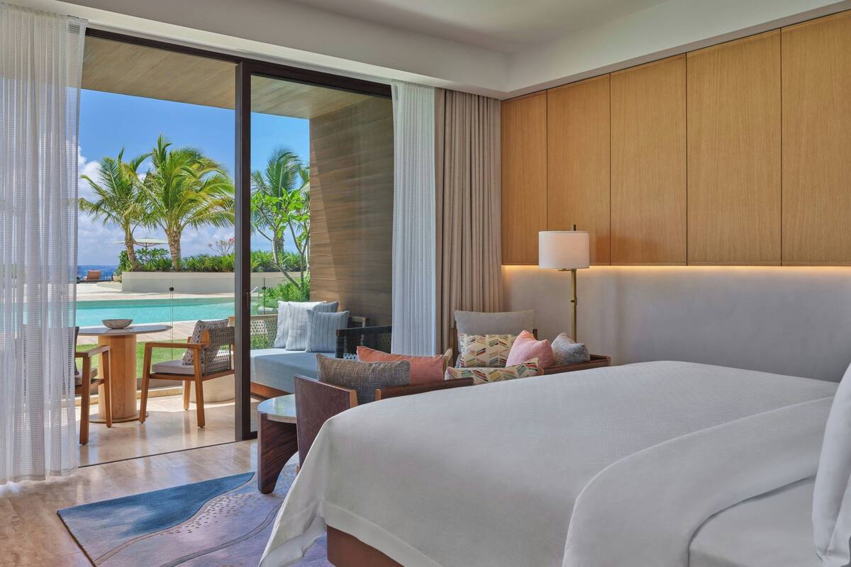 A hotel room with a large bed, a desk, and a view of a pool and palm trees.