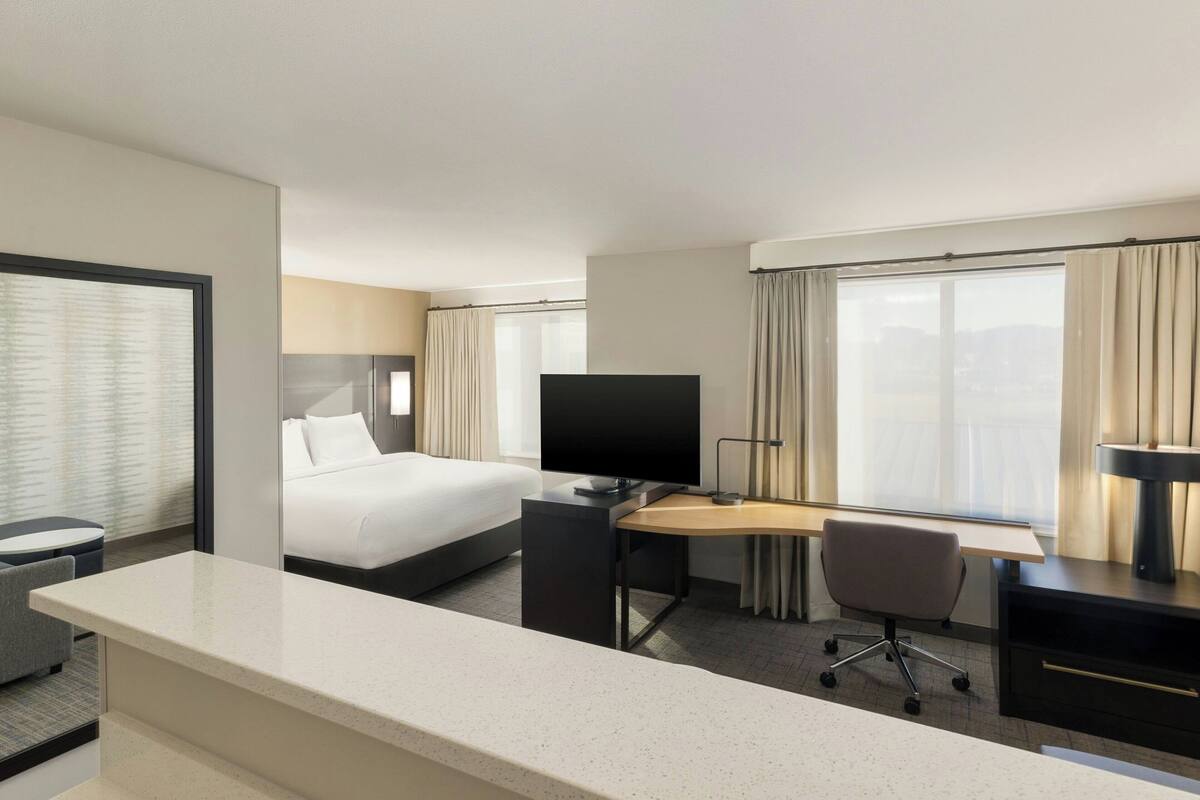 A hotel room with a bed, a desk, a TV, and a window with curtains.