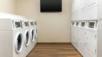A laundry room with multiple washing machines and dryers, a flat-screen TV mounted on the wall, and wooden flooring.