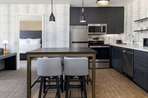 Una habitación de hotel moderna con zona de comedor separada, cama, escritorio y kitchenette.