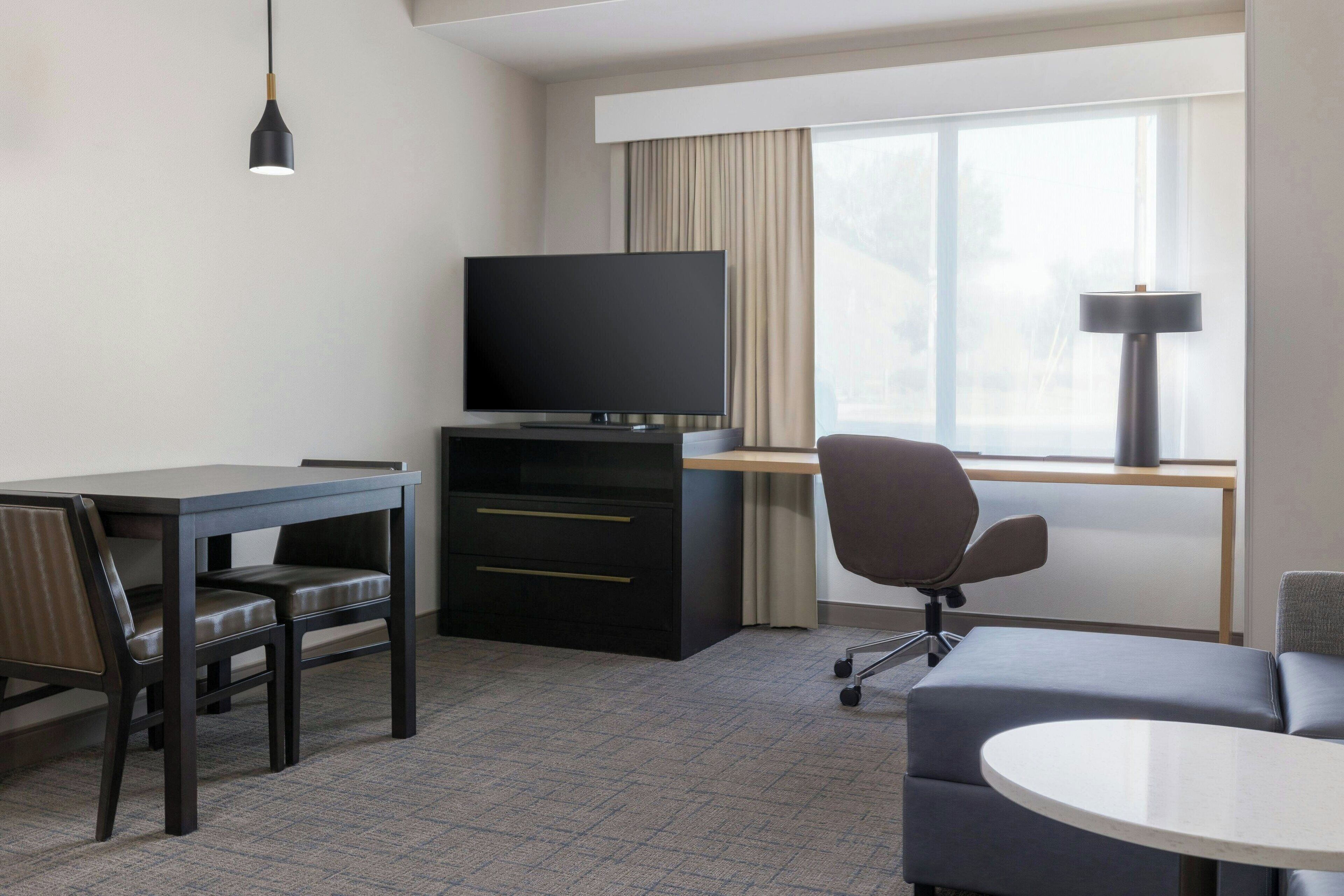A hotel room with a flat-screen TV, a desk, a chair, a sofa, and a lamp.
