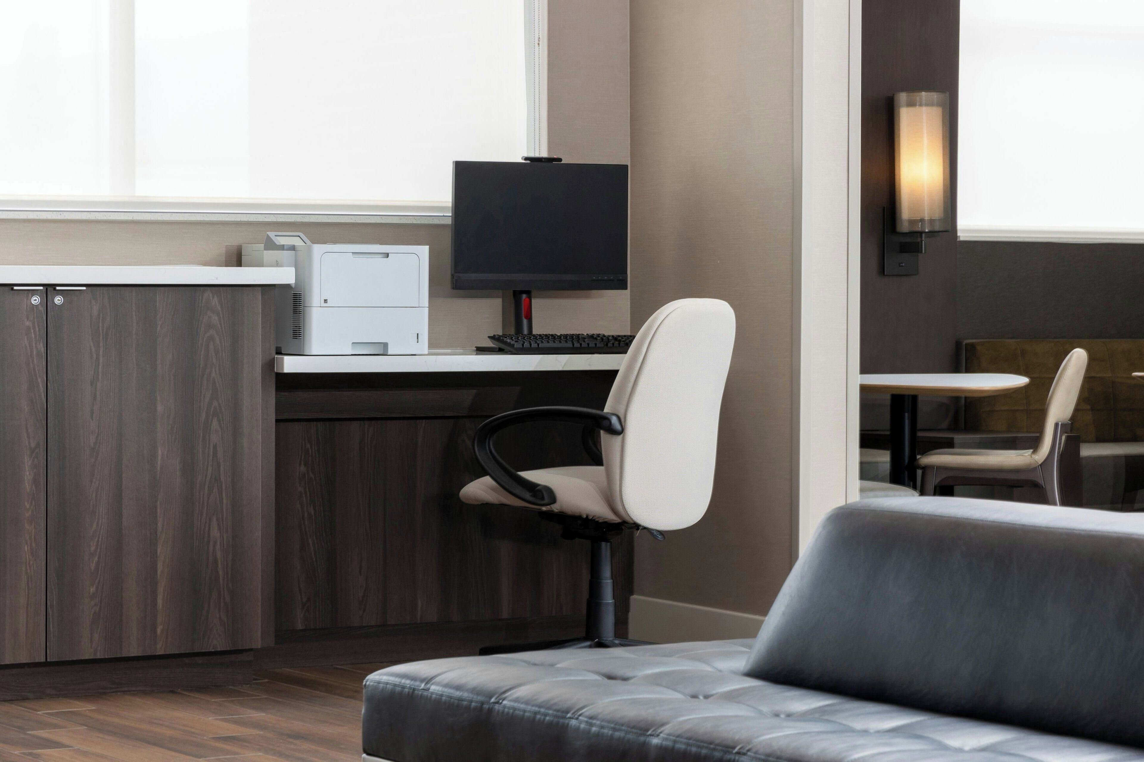 A modern office space with a desk, computer, and chair. There is a sofa and a dining area in the background.