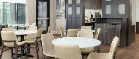 Een moderne eetruimte met ronde tafels en comfortabele stoelen, een keuken met donkerhouten kasten, en een uitzicht op de stad door grote ramen.