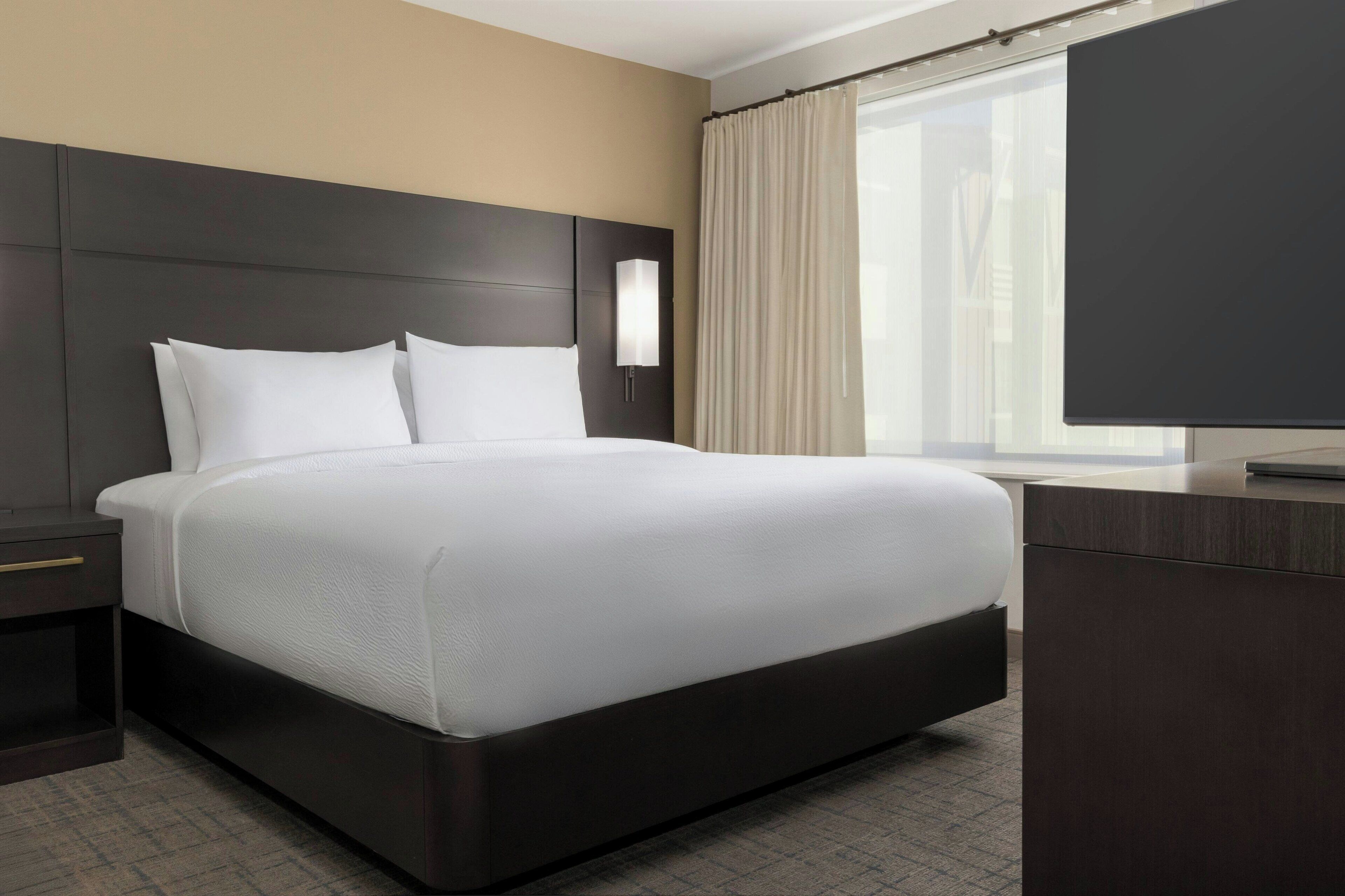 Een moderne hotelkamer met een groot bed, een nachtkastje, een bureau en een televisie.