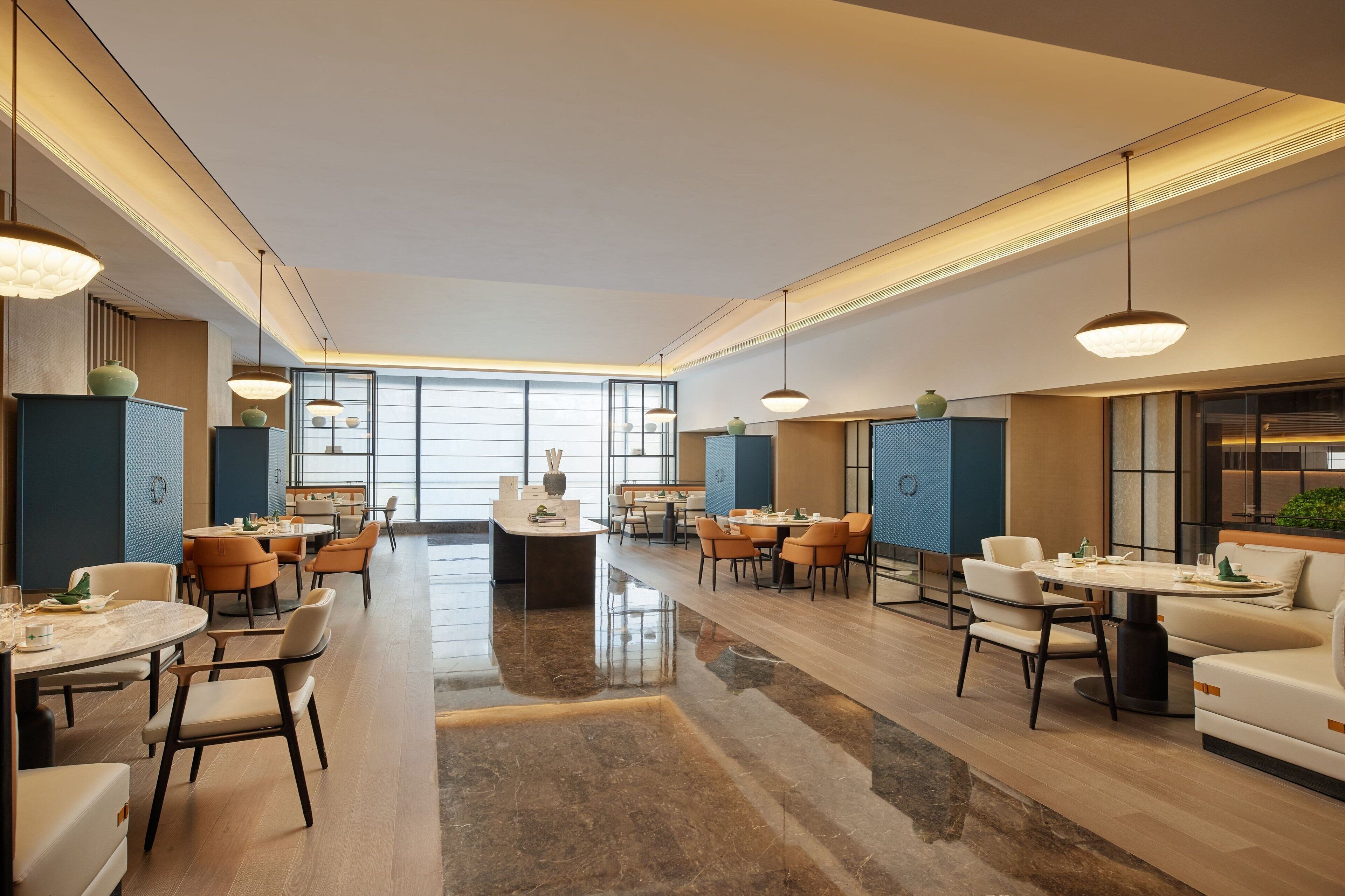 A spacious hotel lobby with multiple dining areas, large windows, and modern lighting fixtures.