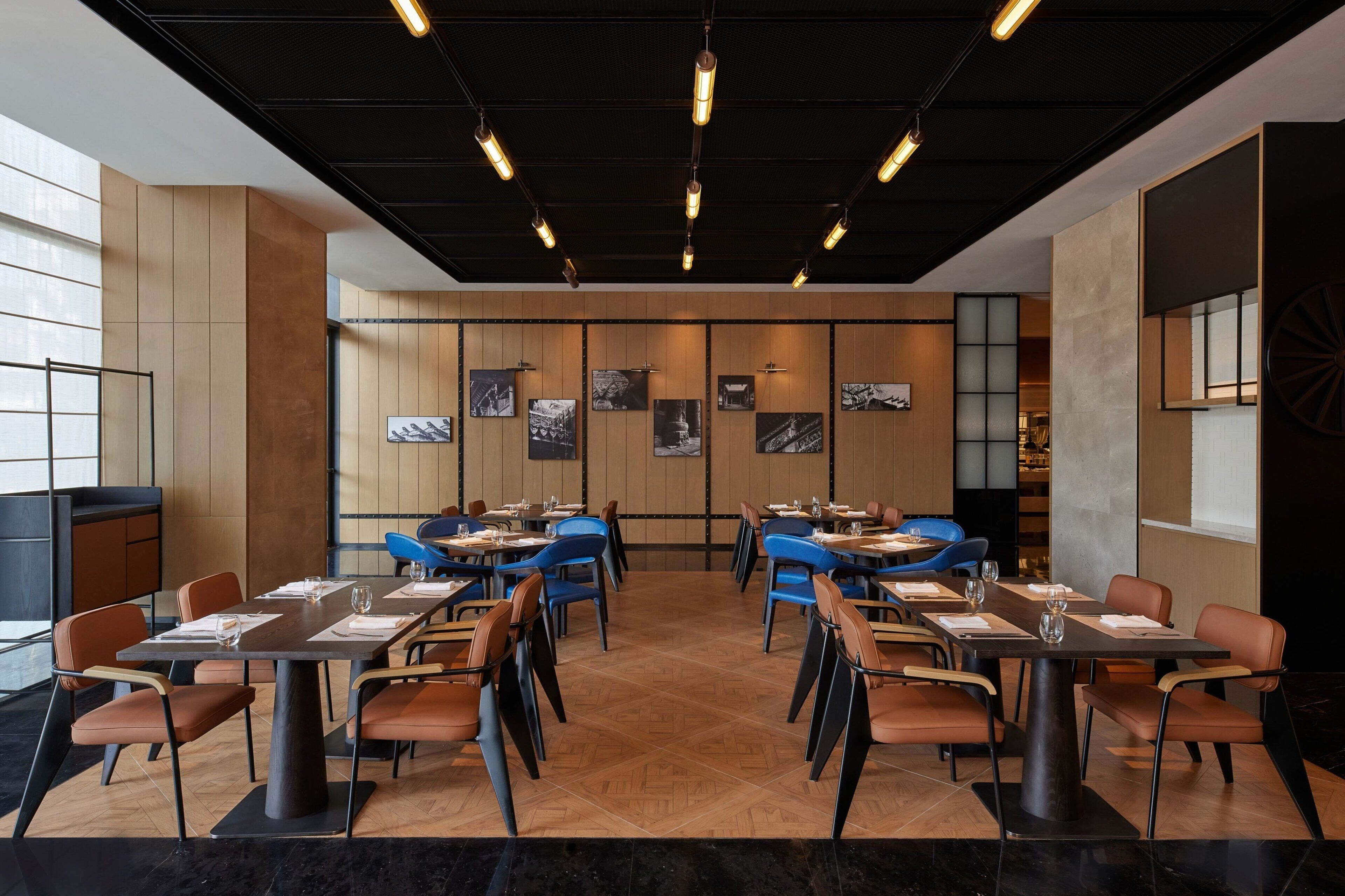 Un ristorante moderno con una sala da pranzo centrale, tavoli e sedie, un pavimento in legno e opere d'arte alle pareti.