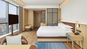 Una habitación de hotel moderna con una cama grande, un escritorio, una silla, un televisor y vistas a la ciudad.