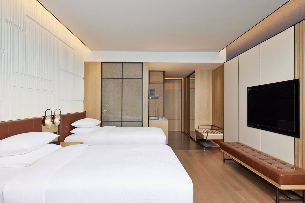 Una habitación de hotel moderna con una cama grande, un televisor y un banco.