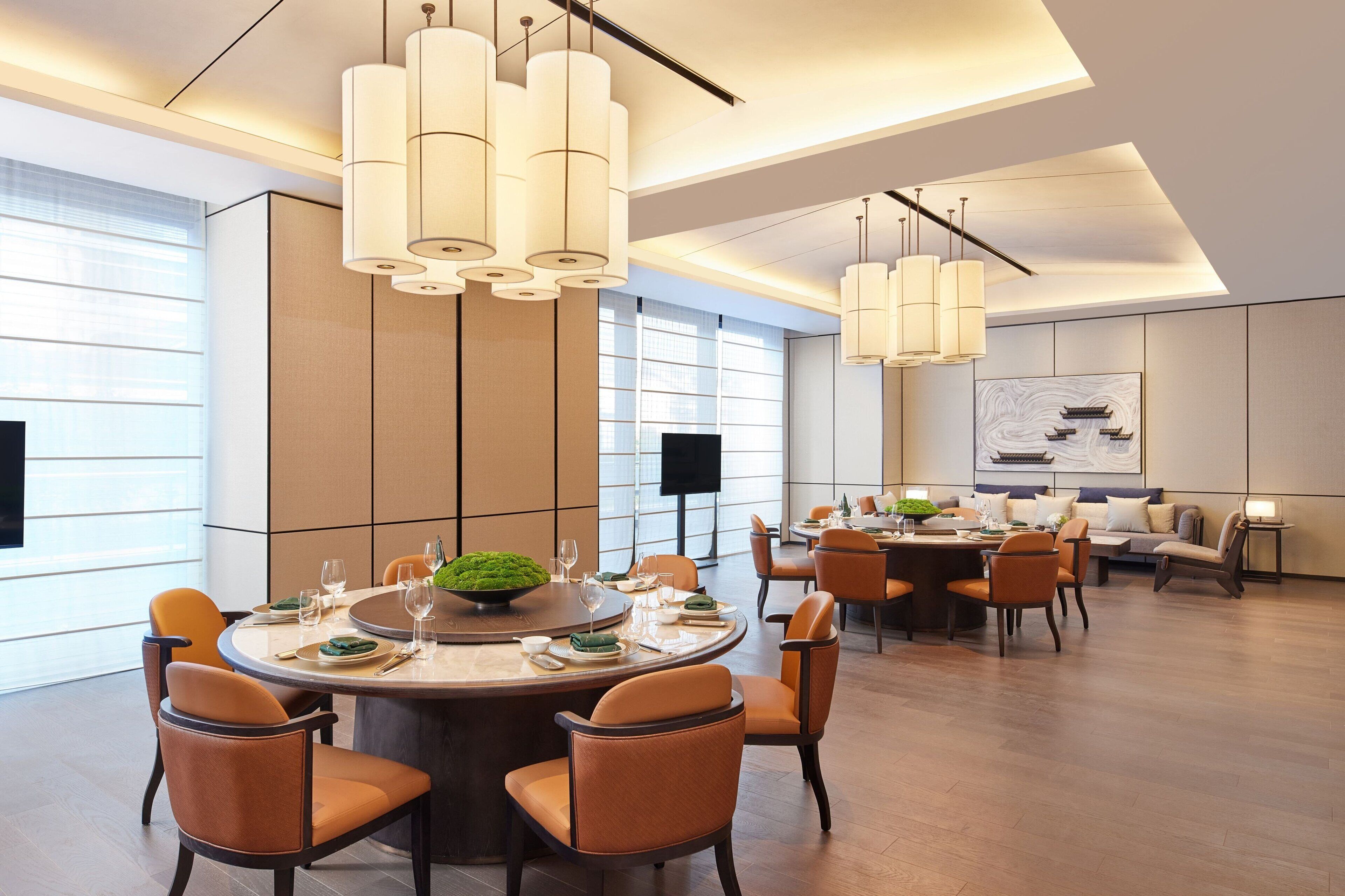 Un espace de salle à manger moderne avec une table ronde, des chaises orange et des luminaires suspendus.