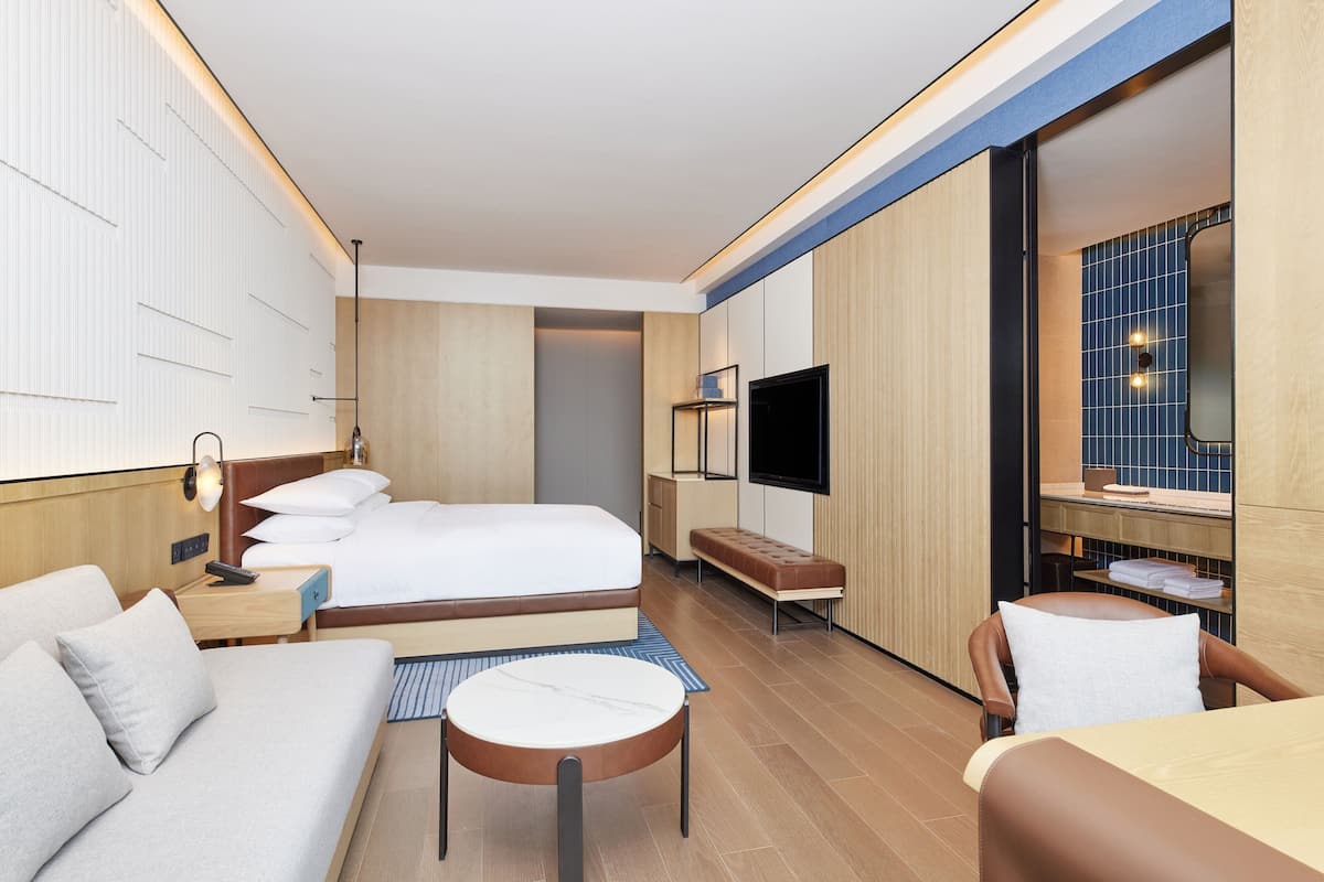 Una habitación de hotel moderna con cama, sofá, sillón, televisión y una mesita.