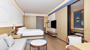 Een moderne hotelkamer met een bed, een bank, een fauteuil, een televisie en een kleine tafel.