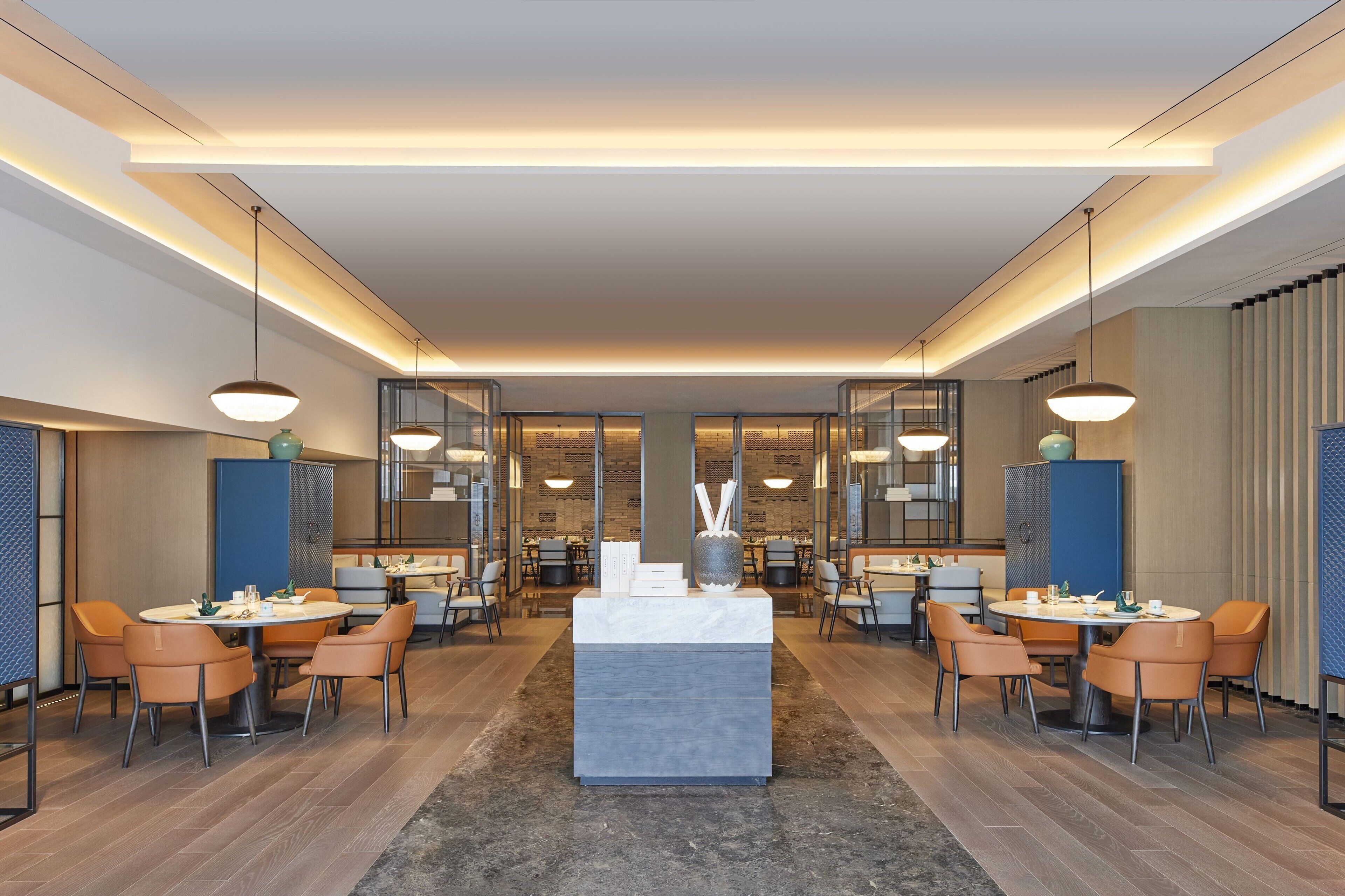 A modern hotel lobby with a central reception desk, multiple seating areas, and a large mirror reflecting the space.