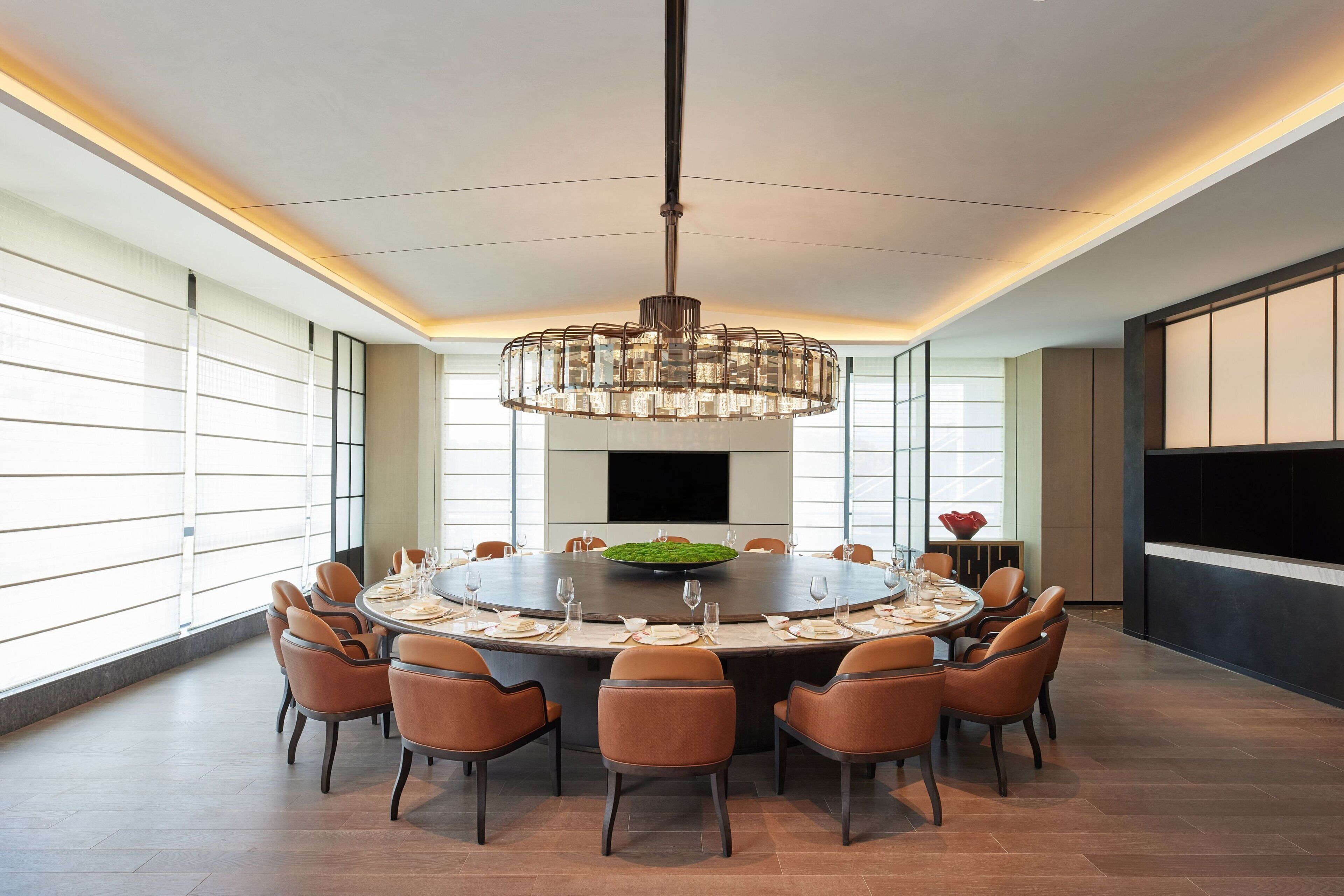 A modern dining area with a round table, chairs, and a central light fixture.