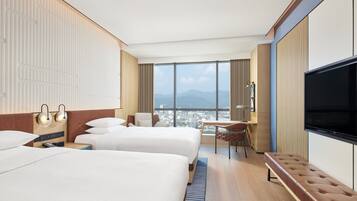 Habitación de hotel con dos camas, televisión, escritorio y vista a la ciudad.