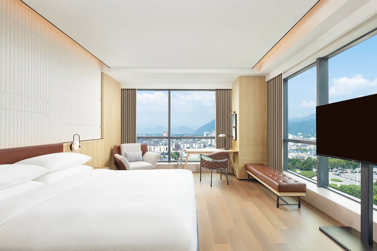 Habitación de hotel con una cama grande, un escritorio, una silla, un banco y un televisor.