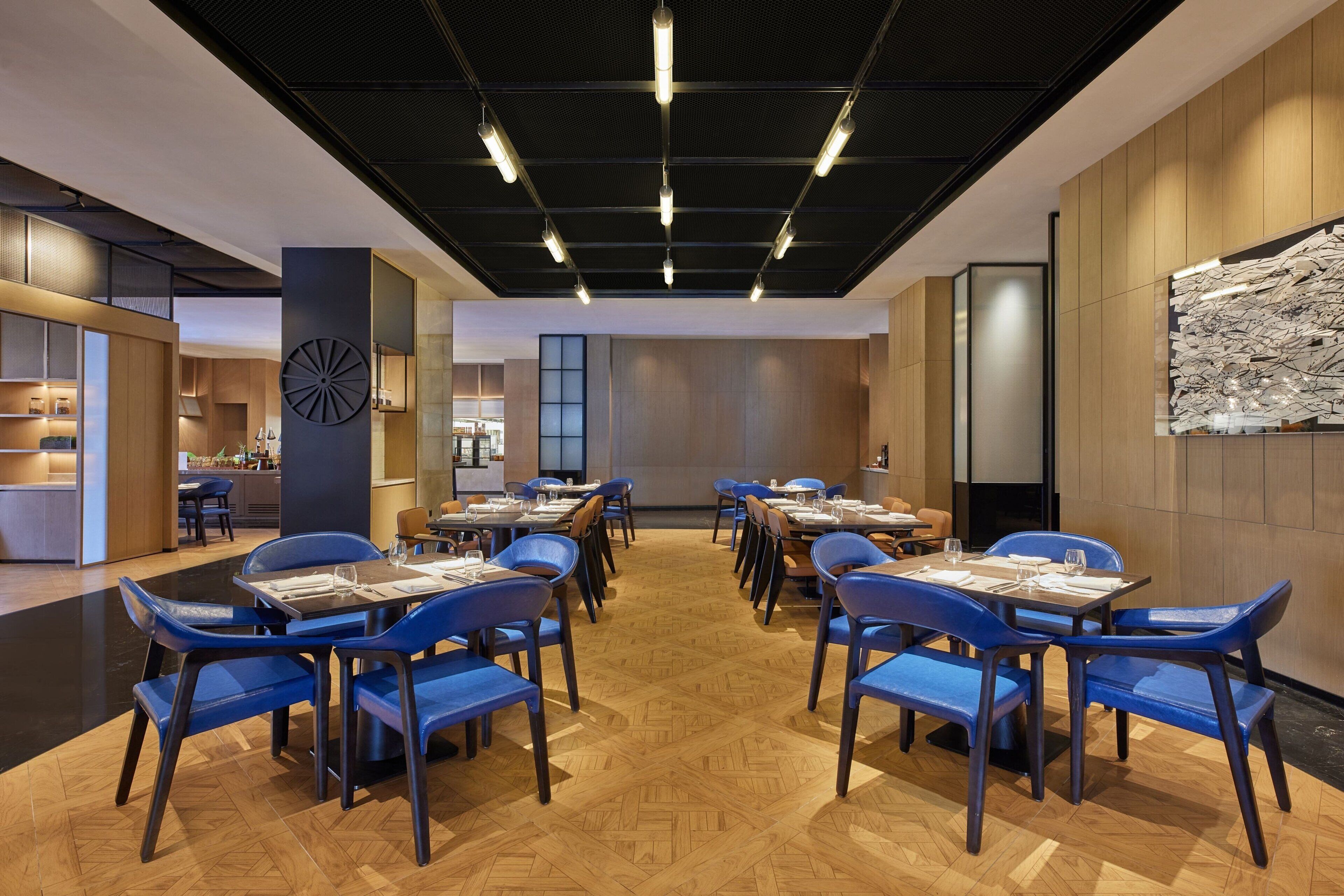 Un comedor moderno con suelo de madera, sillas azules y mesas dispuestas para comer.