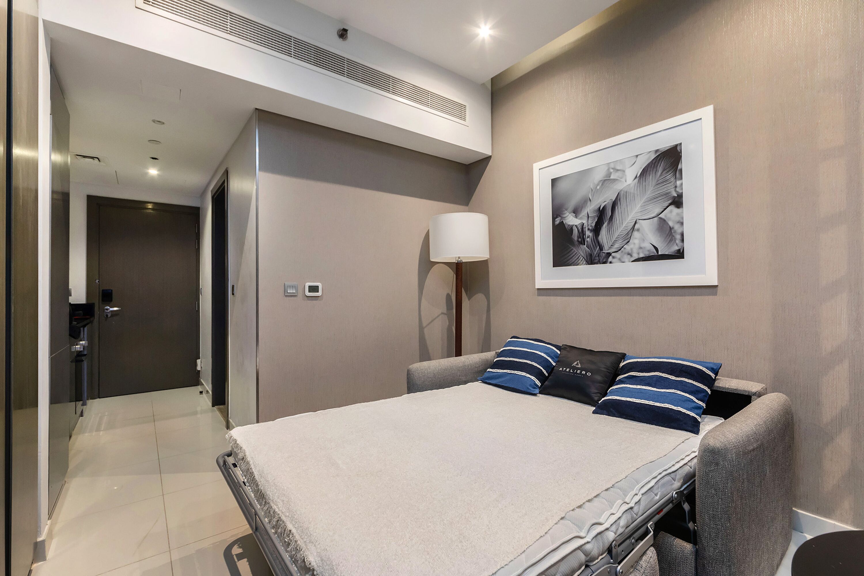 A modern hotel room with a bed, a framed picture on the wall, and a lamp.