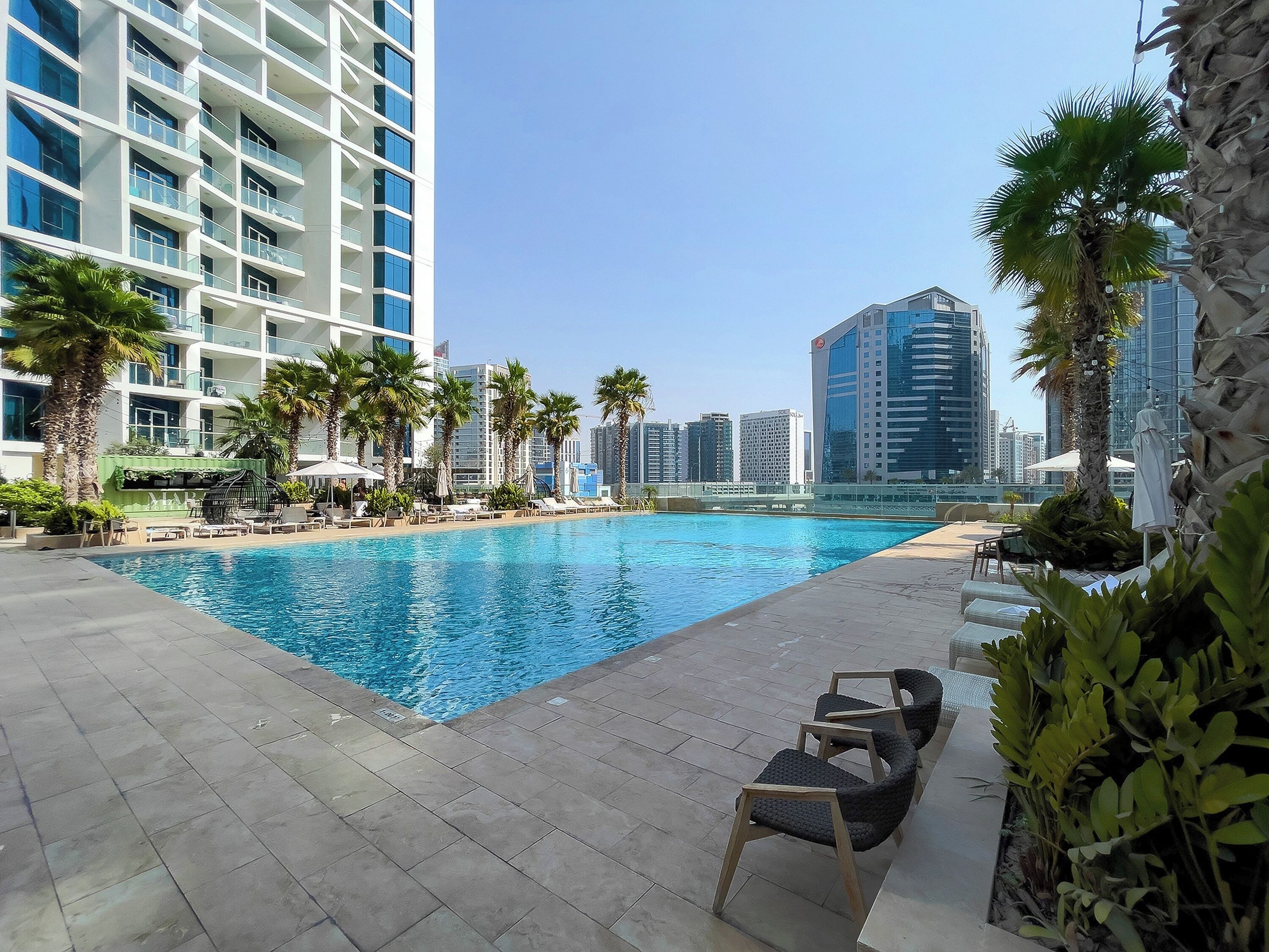 A swimming pool with lounge chairs and palm trees, surrounded by high-rise buildings.