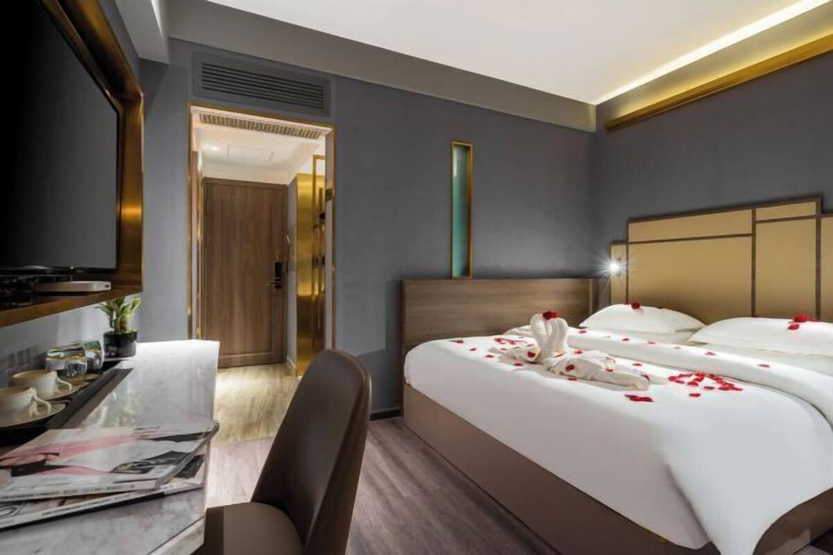 A hotel room with a large bed, a desk with a chair, a television, and a mirror.