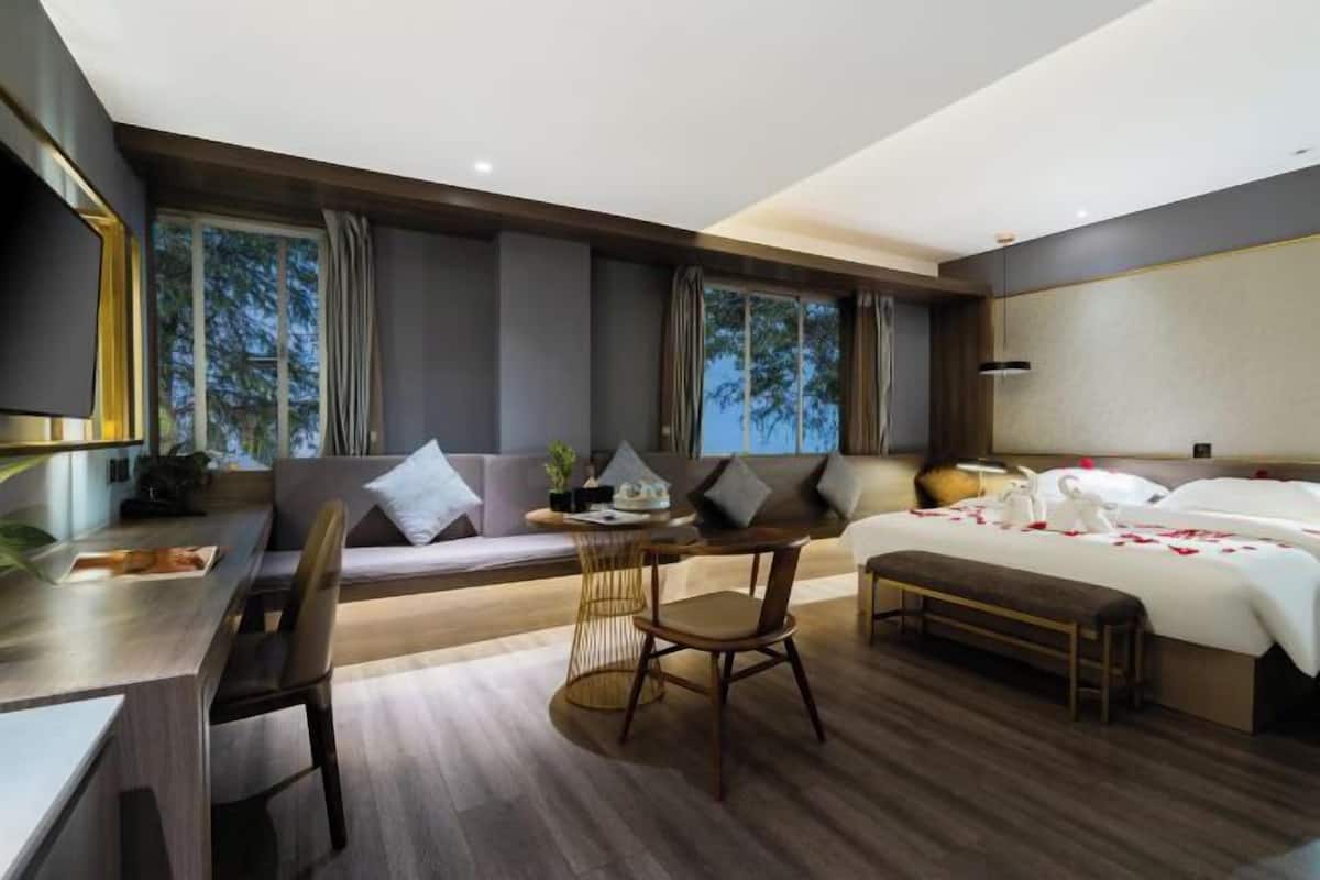 A modern hotel room with a bed, a desk, a chair, a sofa, and a window with curtains.