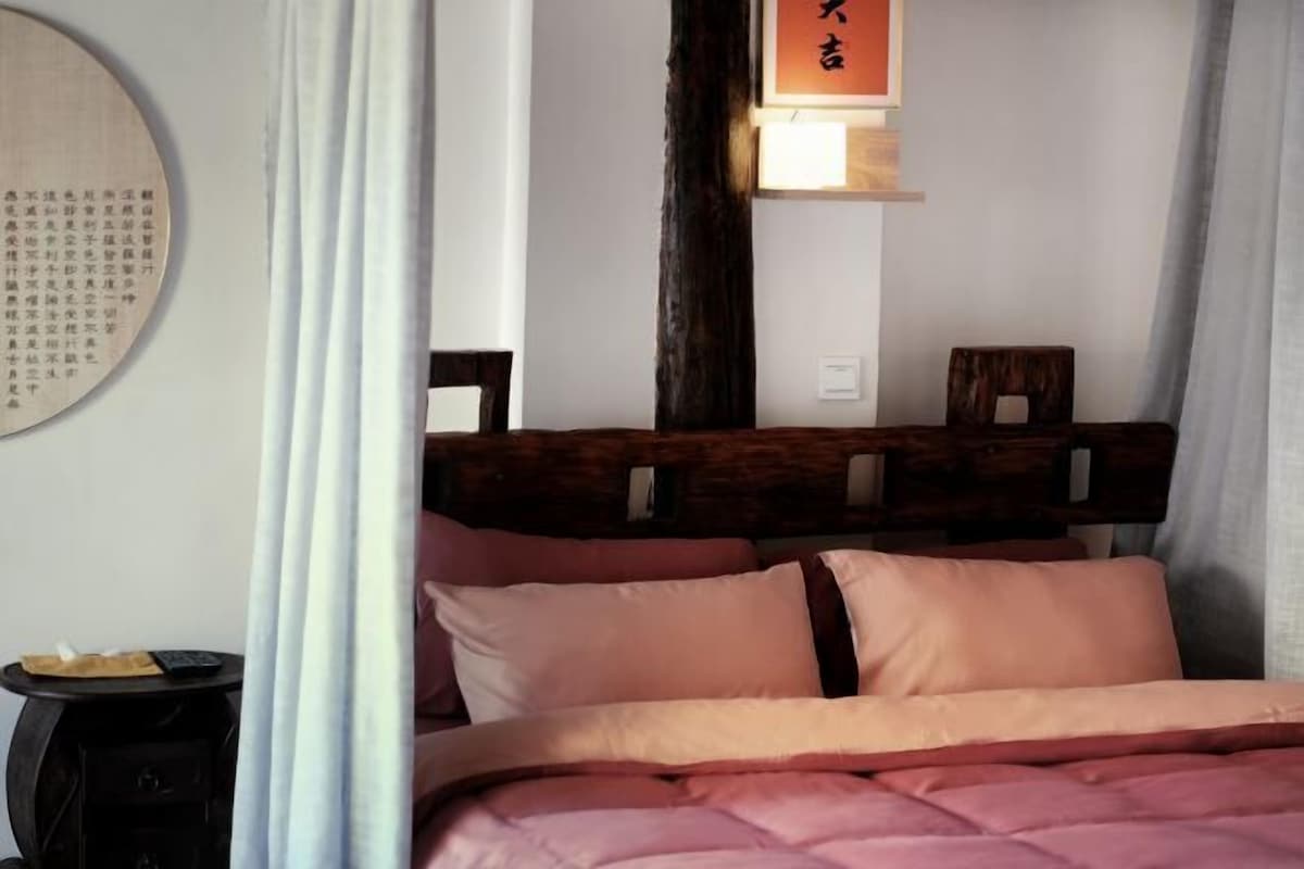A bed with a wooden headboard, a bedside table with a remote control, and a wall-mounted sign with Chinese characters.