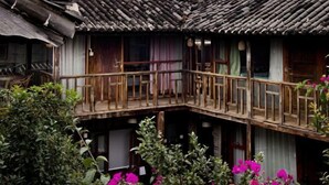 A traditional wooden building with a balcony and a garden with pink flowers. - FullMoon Inn (Lijiang)